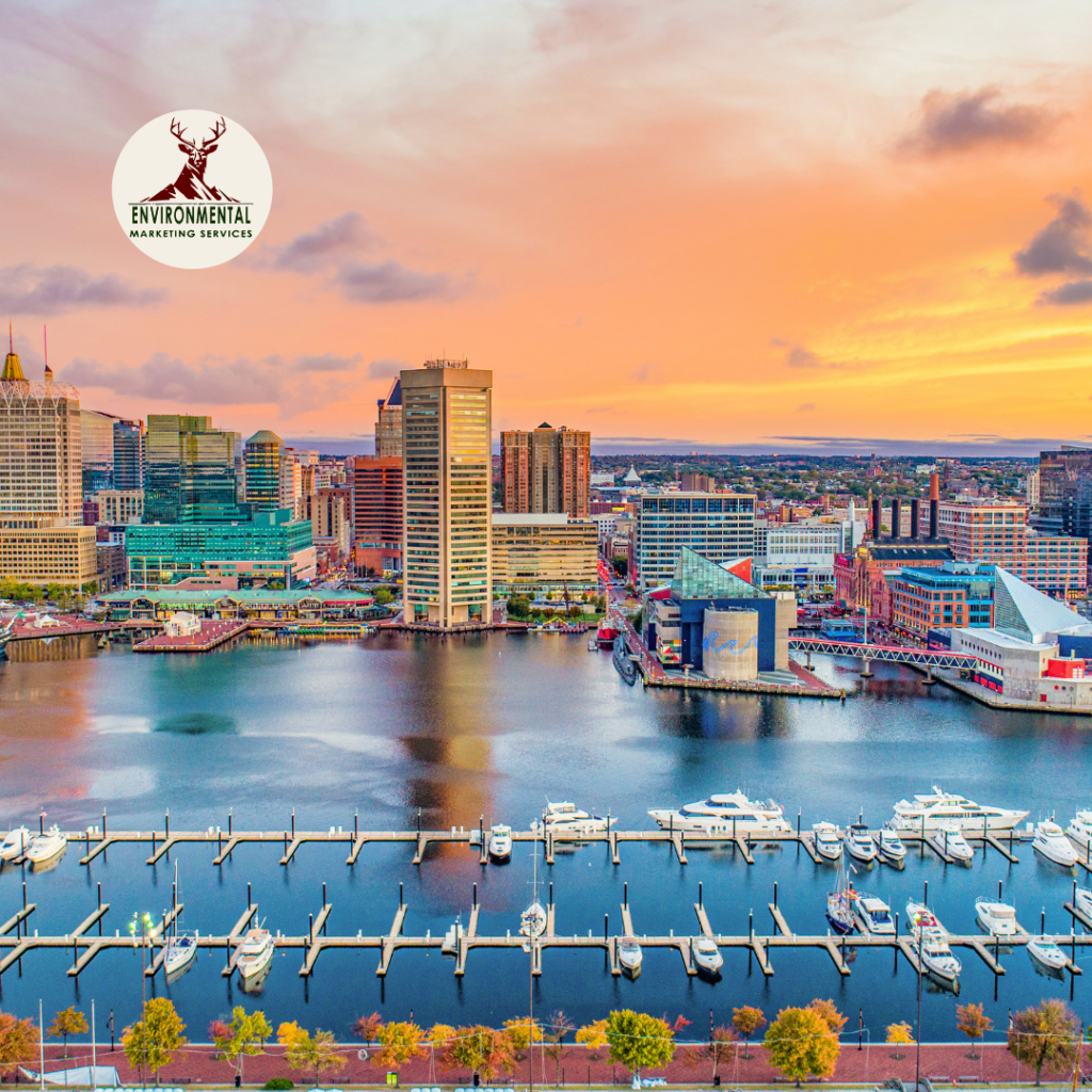 Aerial view of a waterfront city at sunset, featuring buildings and boats in the harbor.